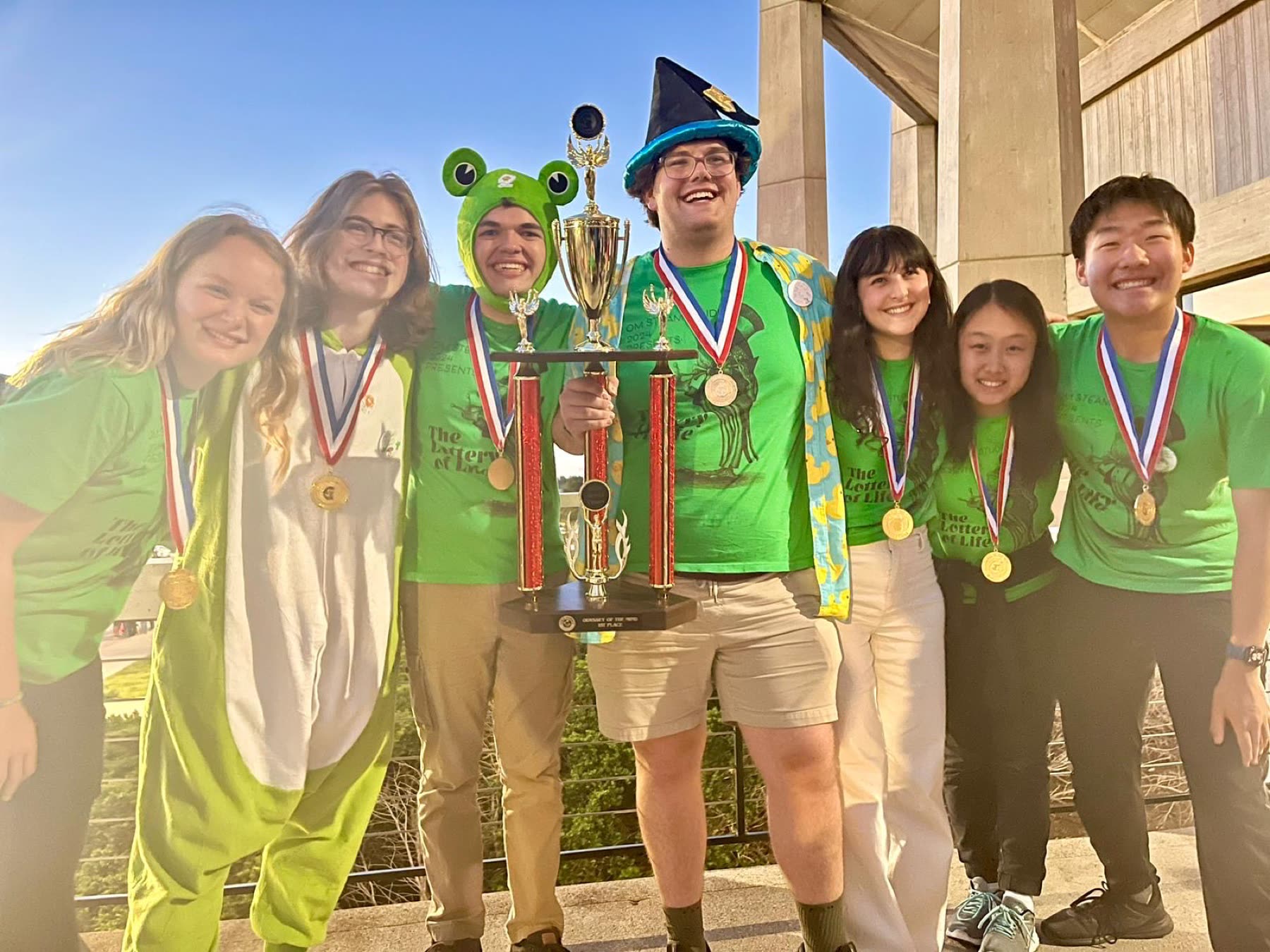 The STEAM Studio Odyssey of the Mind team in green shirts, wearing medals and holding the first-place trophy at the 2024 World Finals